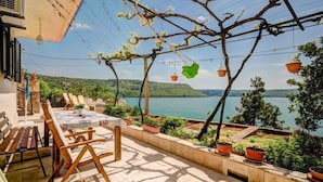 Una terraza con mesa, sillas y plantas en macetas, con vista a un lago.