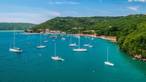 Una zona costera con numerosos veleros anclados en aguas turquesas, rodeada de exuberantes colinas verdes y un pequeño asentamiento.