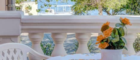 Un balcón con barandilla blanca, una mesa con mantel floral y una maceta con flores naranjas.
