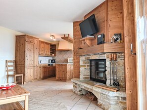 A kitchen with wooden cabinets, a stone fireplace, a television, and a microwave.