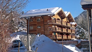 Una xalet de fusta amb nombrosos balcons, envoltat d'arbres coberts de neu i un cel blau clar.