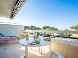 Un balcon avec une table préparée pour le petit-déjeuner, comprenant des croissants, une bouteille de jus d’orange et un bol vert.