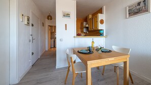 Ein Essbereich mit Holztisch und -stühlen, im Hintergrund eine Küche und ein Flur, der in einen weiteren Raum führt.