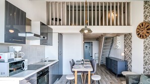 Eine moderne Küche mit Essbereich, einem Schlafzimmer im oberen Bereich und einem Wohnzimmer mit Sofa und Uhr.