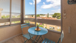 A balcony with a table and chairs, a potted plant, and a view of buildings and trees.