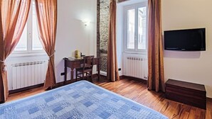 A bedroom with a bed, a desk, a chair, a television, and a stone wall. - Domus Fori by Interhome (Rome: Historical City Center)