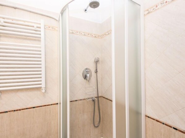 Eine Dusche mit Glastür, Handbrause und Wandarmatur.
