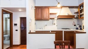 A compact kitchen with wooden cabinets, a gas stove, and a dining area with a table and chairs. - Domus Fori by Interhome (Rome: Historical City Center)