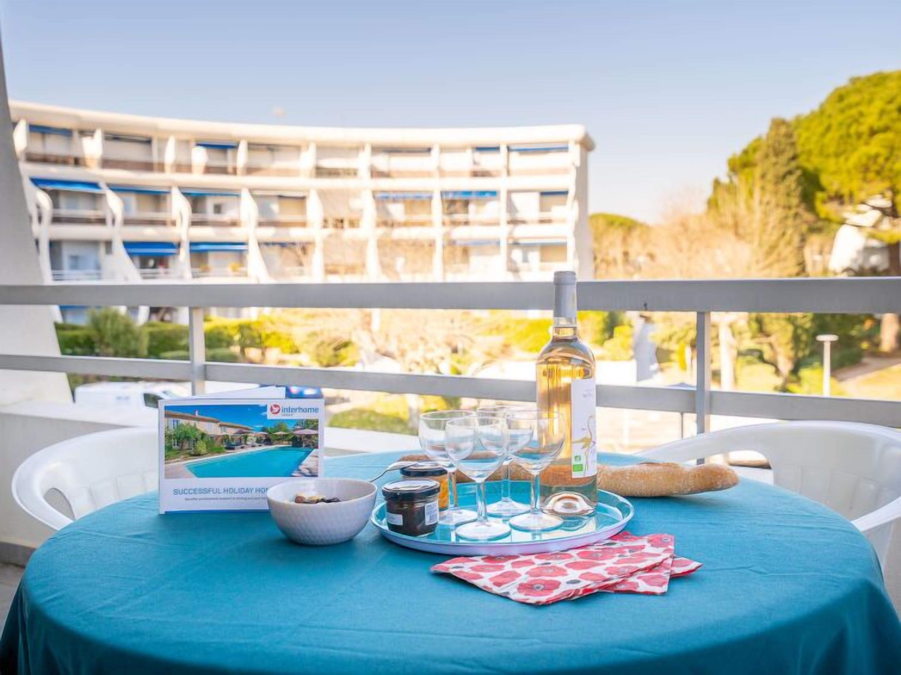 Une table dressée avec une bouteille, des verres, un bol et un plateau contenant des condiments, donnant sur un immeuble doté de balcons et de verdure.