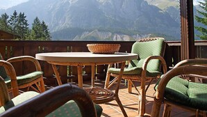 A terrace with wicker furniture and a table, overlooking a mountain range. - Chalet Marietta by Interhome (Kandersteg)