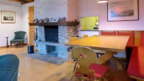 A dining area with a stone fireplace, wooden beams, and a large table. - Chalet Marietta by Interhome (Kandersteg)