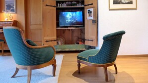 A cozy living room with two teal upholstered chairs, a wooden entertainment unit with a television, and a framed picture on the wall. - Chalet Marietta by Interhome (Kandersteg)