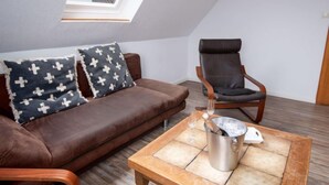 Un soggiorno accogliente con un divano in pelle marrone, due cuscini decorati, una poltrona a dondolo in legno e un tavolino con un contenitore metallico.
