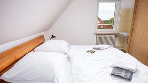 Letto rifatto con cura in una stanza con soffitto spiovente, una finestra vista case e un termosifone.