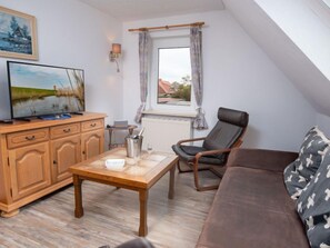Ein gemütliches Wohnzimmer mit einem Holztisch, einem Ledersessel, einem braunen Sofa und einem Fernseher auf einer Holzkommode.