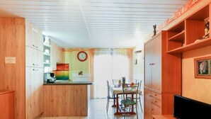 Een kleine keuken met houten kastjes, een eethoek met een tafel en stoelen, en een televisie op een houten dressoir.