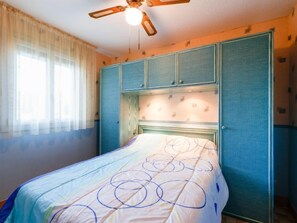 Een slaapkamer met een bed, een plafondventilator en een kledingkast.