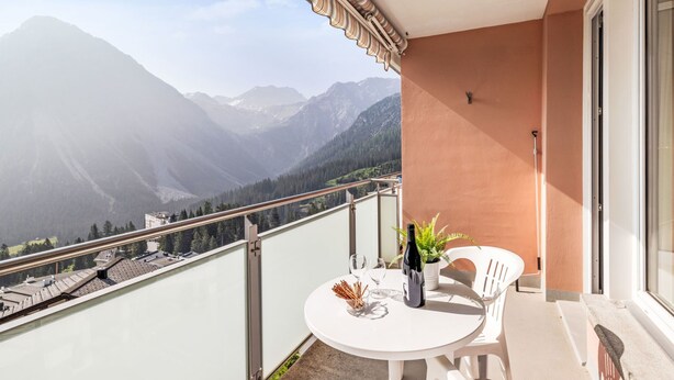 Un balcon avec une table et des chaises, donnant sur un paysage montagneux.