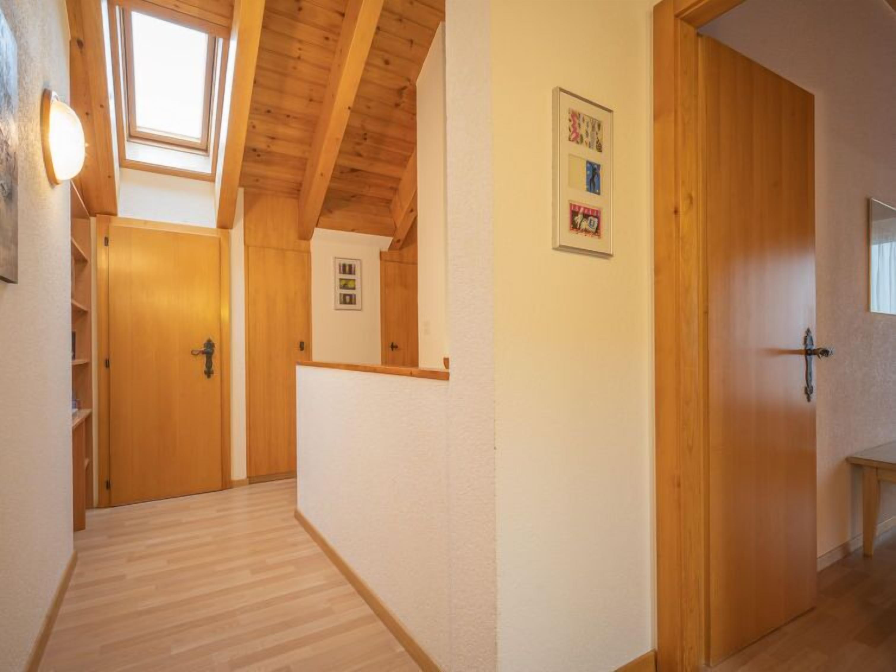 Un couloir étroit avec un plancher et des murs en bois, une lucarne et une porte dotée d’une petite fenêtre.