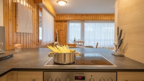 Une cuisine moderne avec un lambris en bois, une cuisinière encastrée et un coin repas comprenant une table et des chaises.
