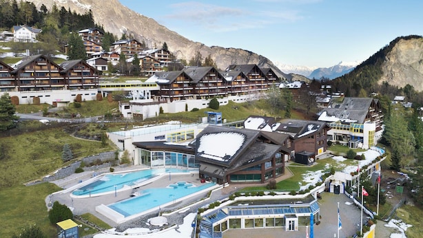Une station de montagne comprenant plusieurs bâtiments de style chalet, une piscine et un télésiège.