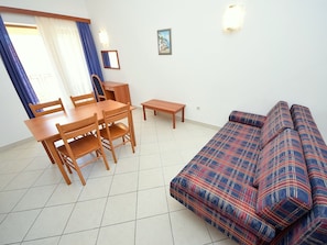 Una sala de estar con un sofá, una mesa de comedor con sillas y una mesita.