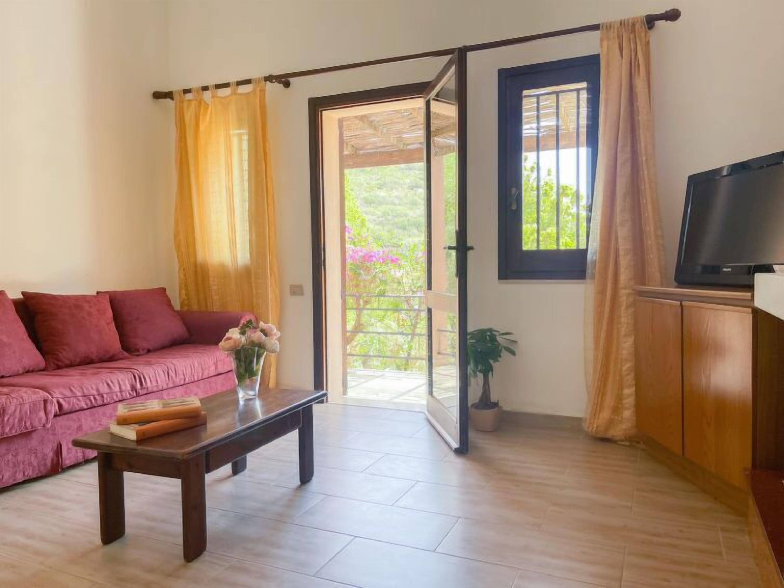 A living room with a sofa, a coffee table, a TV, and a sliding glass door leading to a balcony.