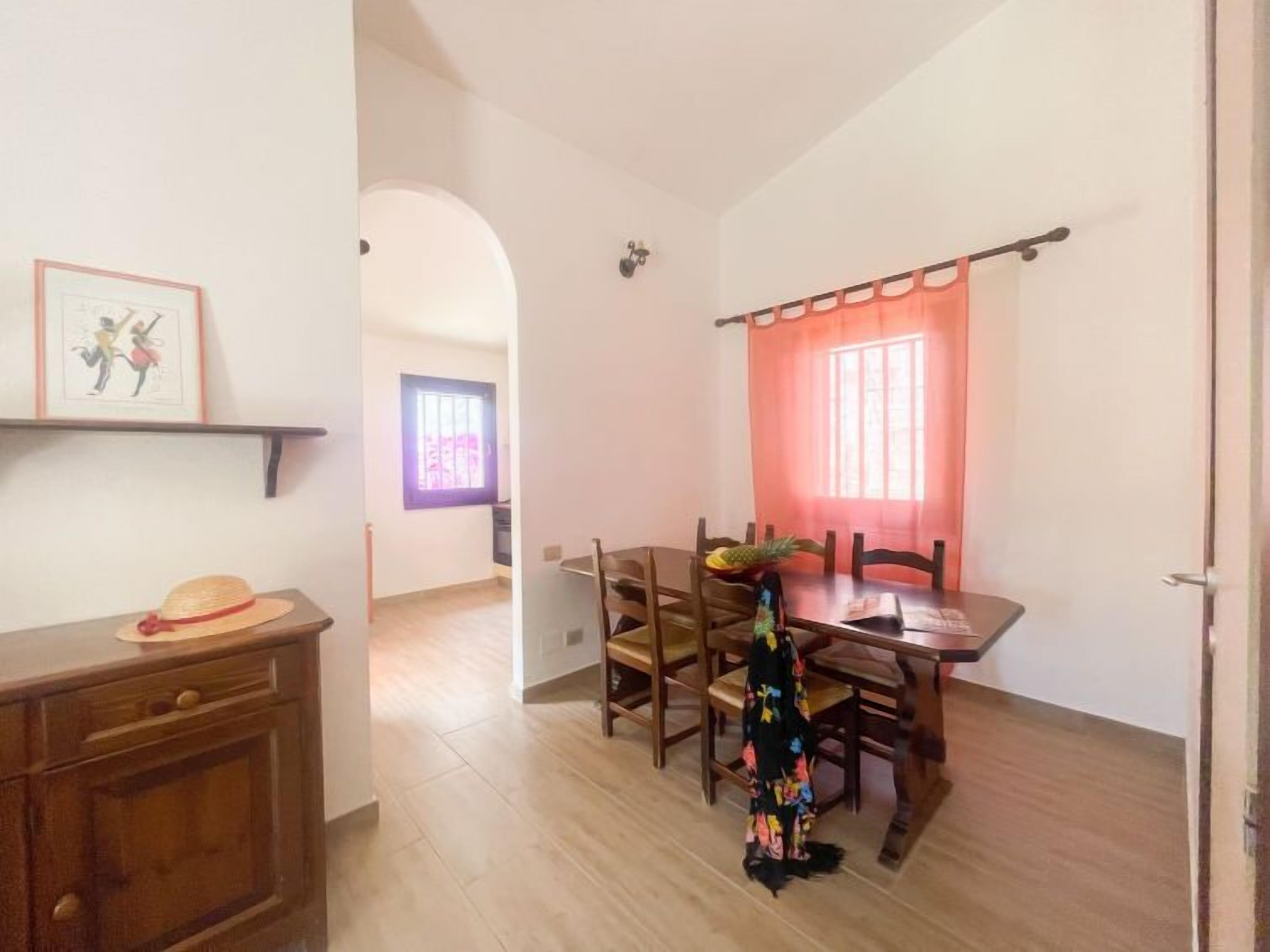 A dining area with a wooden table and chairs, a red curtain, and a pineapple on the table.