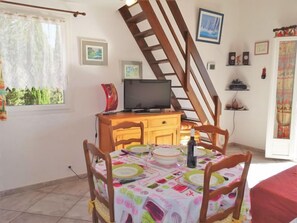 A dining area with a table set for two, a television on a wooden cabinet, and a staircase in the background. - Les Romarines by Interhome (Gruissan)