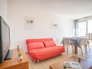 Uma sala de estar moderna com um sofá vermelho, uma mesa de jantar com cadeiras e uma televisão sobre um móvel de madeira.