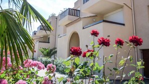 A multi-story building with balconies, a palm tree, and flowering plants. - Les Embruns by Interhome (Saint Cyprien)