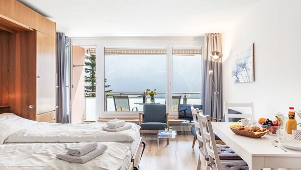 Een hotelkamer met twee bedden, een eettafel met stoelen, een televisie en een balkon met uitzicht.