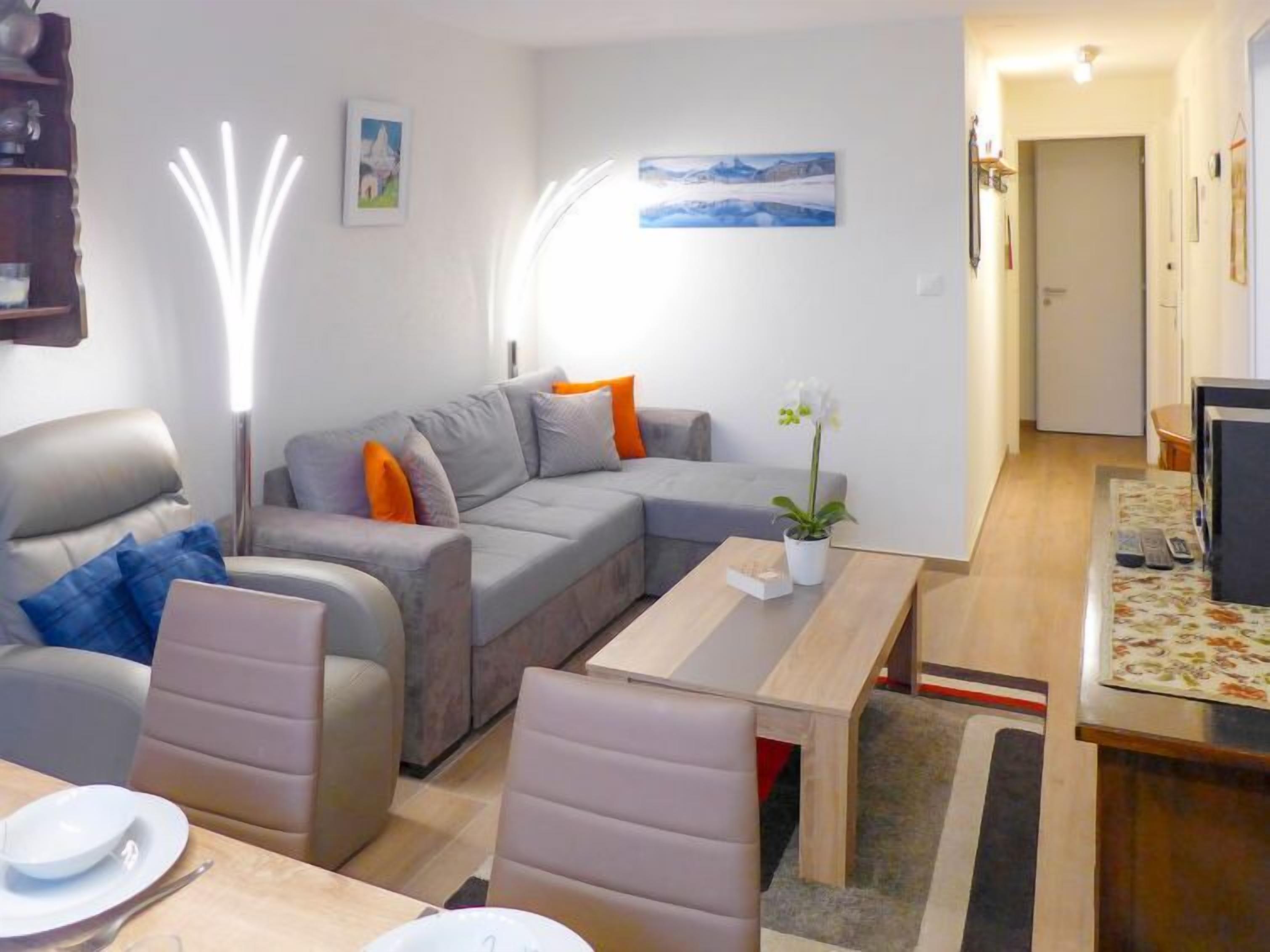 Un salon moderne avec un canapé gris, une table basse en bois et un coin repas avec une table dressée pour deux personnes.