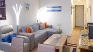 A modern living room with a grey sofa, a wooden coffee table, and a dining area with a table set for two. - Barzettes-Vacances 553 / Entrée N° 14 by Interhome (Crans-Montana)