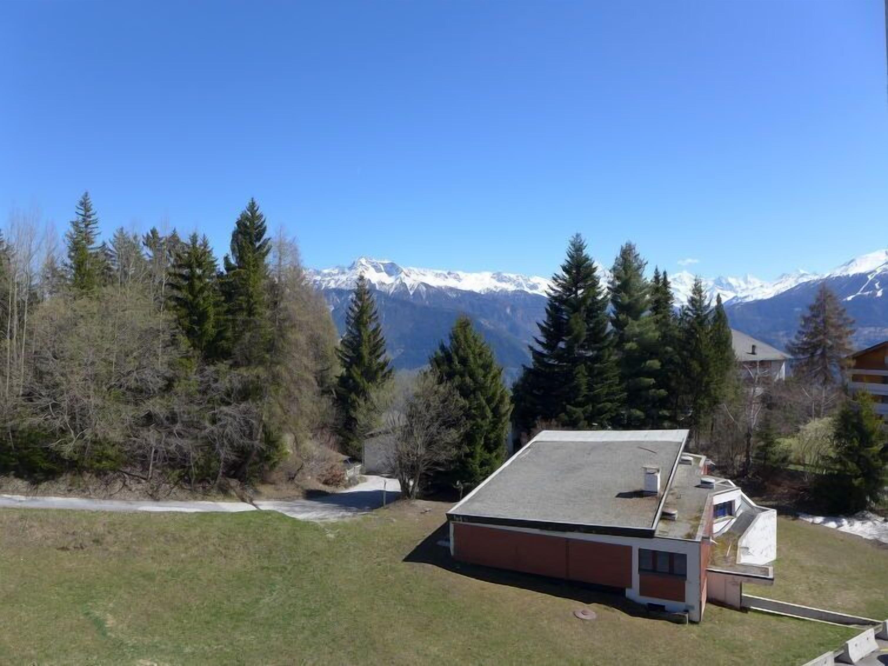 A building with a sloped roof, surrounded by trees and a mountain range in the background.