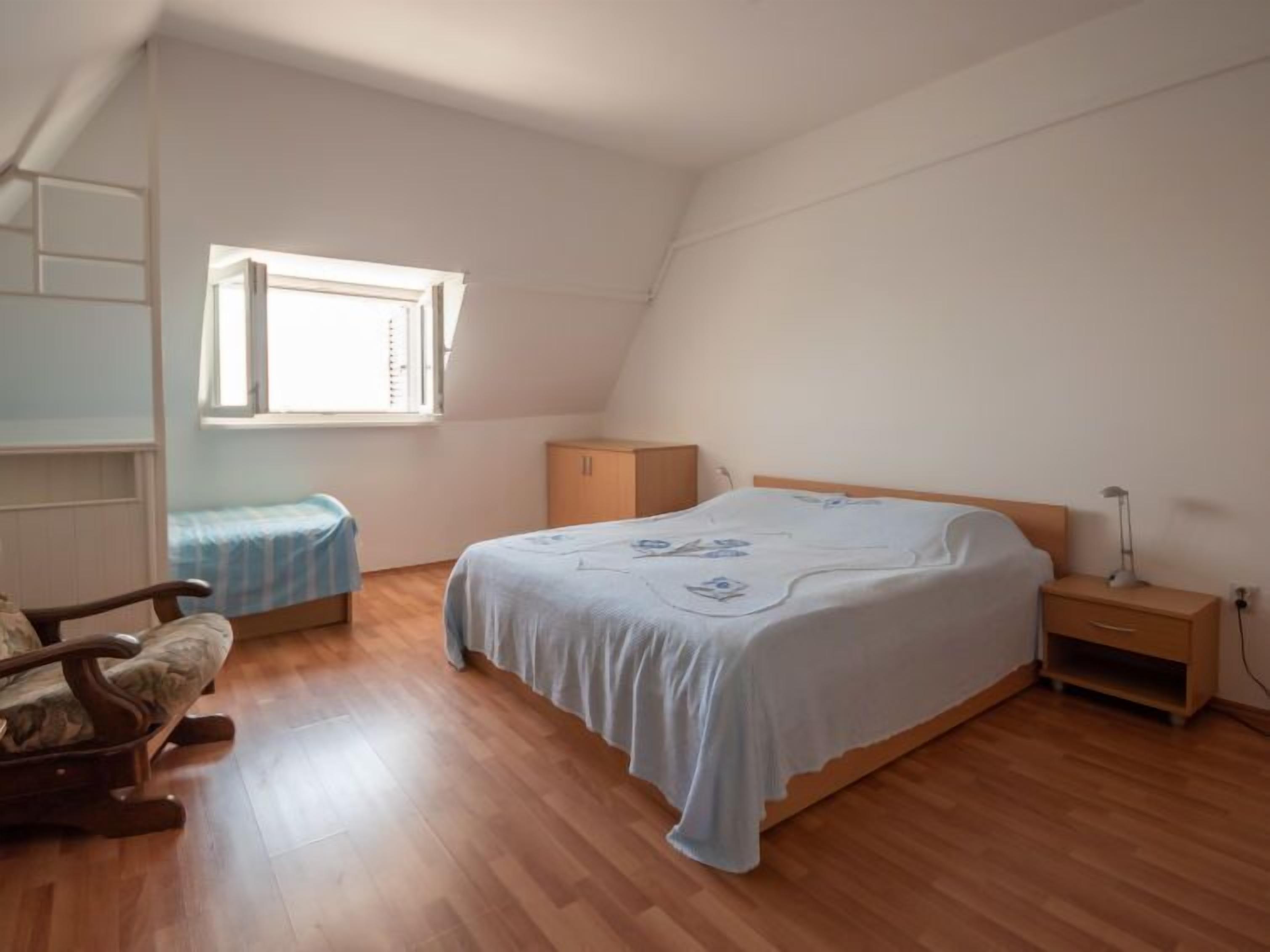 Una camera da letto con un letto singolo, un comodino in legno, una sedia, una piccola credenza e una finestra.