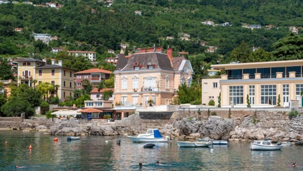 Une ville côtière dotée d’un port de plaisance, de bâtiments historiques et d’un paysage vallonné en arrière-plan.