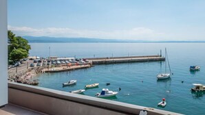 Un port de plaisance avec des bateaux amarrés, une jetée et une vue dégagée sur l’eau et les montagnes lointaines.