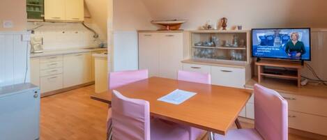 A compact kitchen with white cabinets, a small refrigerator, and a dining area with a wooden table and pink chairs.