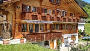 Een houten chalet met balkon, stenen deuropgang en een berg op de achtergrond.