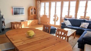 Een gezellige woonkamer met een houten eettafel, een blauwe bank en een groot raam met gordijnen.