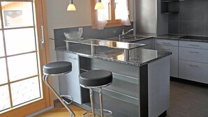 Een moderne keuken met een glazen kookeiland, roestvrijstalen apparatuur en barstoelen.