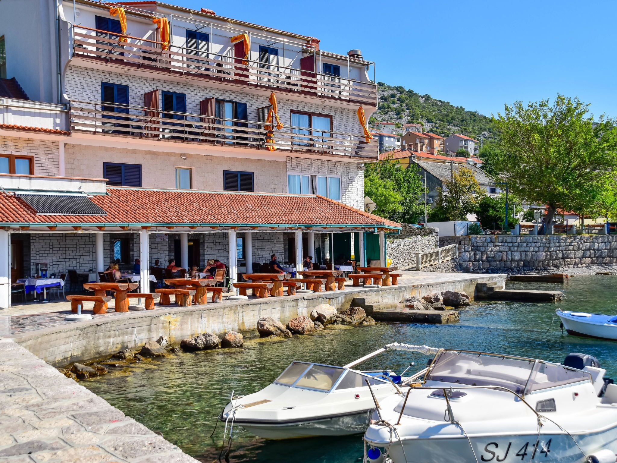 Een restaurant aan het water met terras, een stenen muur en boten in de haven.