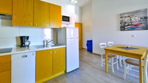 Une cuisine compacte avec des meubles en bois, un lave-vaisselle blanc, un four à micro-ondes et un évier. On y trouve une table à manger avec des chaises et un tableau accroché au mur.
