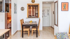 Een eethoek met een tafel voor vier personen, een houten stoel en een bank met een kleurrijk kussen.