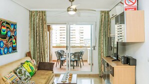 Een woonkamer met een bank, salontafel en een televisie op een houten kast. Er is een balkon met stoelen en een tafel.