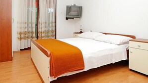 A bedroom with a bed, a nightstand, a television, and a window with curtains.