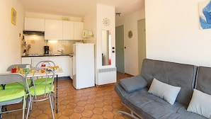 Un espacio habitable compacto con kitchenette, una zona de comedor con mesa y sillas, y un sofá gris.