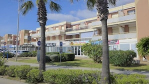 Un edificio de varios pisos con balcones, zona de estacionamiento y palmeras.