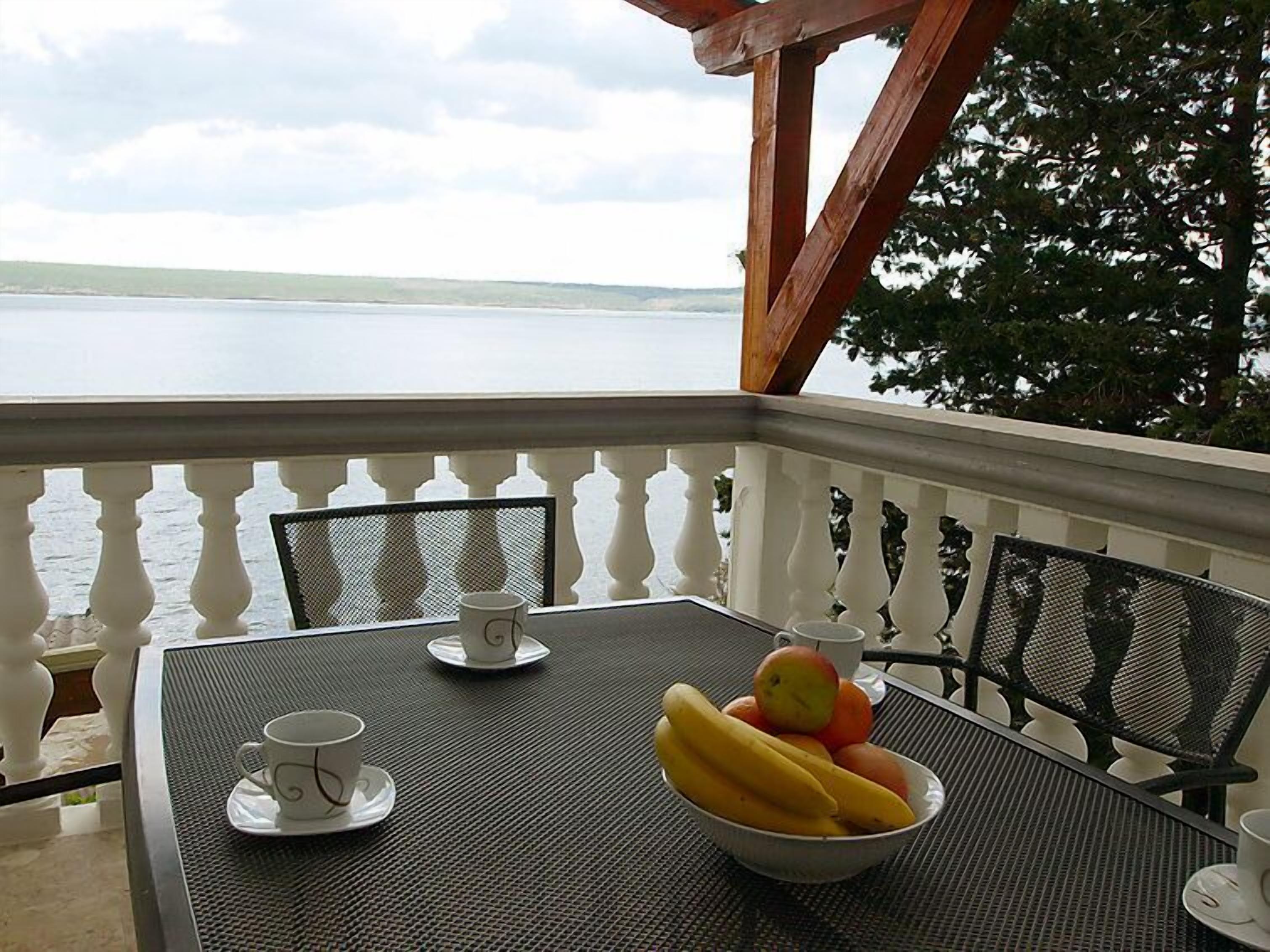 En balkon med et bord dækket til to personer, med en skål frugt og to kopper.